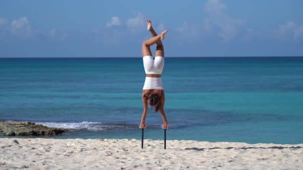 Γυναίκα φορώντας λευκά κάνει handstand στην παραλία με τη θάλασσα. Έννοια της θέλησης, του δυναμικού και της επιθυμίας — Αρχείο Βίντεο