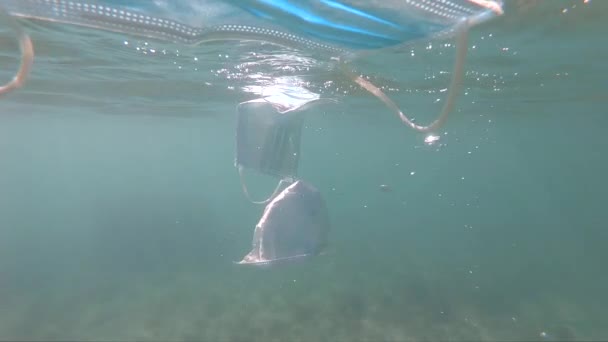 Beschermende gezichtsmaskers tegen het coronavirus dat onder water zweeft. Verontreiniging van het milieu en ecologisch vraagstuk — Stockvideo