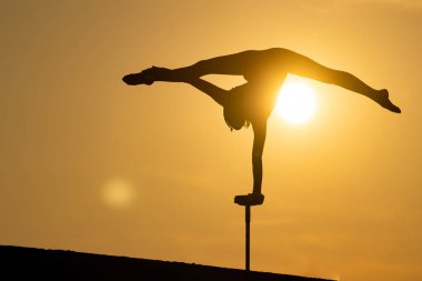 Esnek akrobatın silueti dramatik günbatımı arka planında amuda kalkıyor. İrade, kontrol ve rüya kavramı