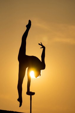Esnek akrobatın silueti dramatik günbatımı arka planında amuda kalkıyor. İrade, kontrol ve rüya kavramı