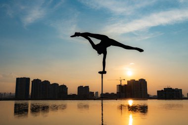 Esnek akrobatın silueti dramatik günbatımı ve şehir manzarası arka planında amuda kalkıyor. Bireysellik kavramı, yaratıcılık ve olağanüstü