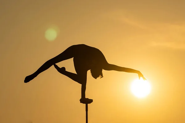 Artista de circo femenino flexible mantener el equilibrio y tocar el sol contra el atardecer dramático. Motivación, pasión y concepto de logro — Foto de Stock