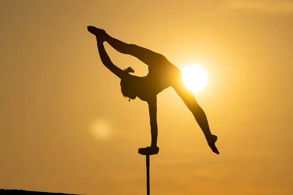 Silueta de circo femenino flexible Artista mantener el equilibrio en una mano en la azotea contra la puesta de sol dramática. Soporte de mano y concepto de equilibrio — Foto de Stock