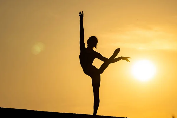 Silueta de chica flexible y en forma manteniendo el equilibrio en división sobre el fondo del atardecer. Concepto de yoga, meditación y estilo de vida saludable — Foto de Stock