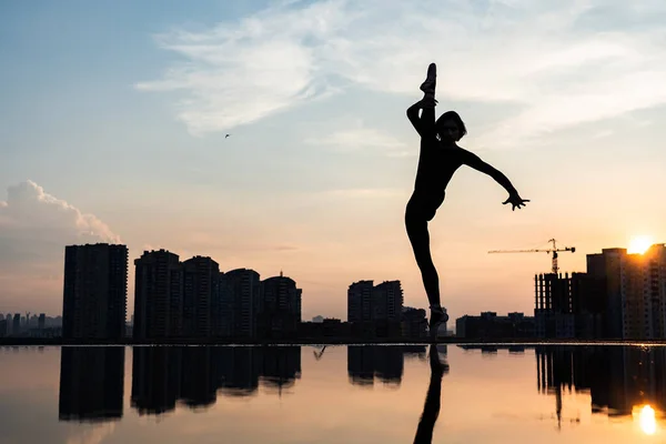 Silueta de bailarina actuando sobre paisaje urbano y dramático fondo de atardecer. Concepto de fuerza de voluntad, control y sueño — Foto de Stock