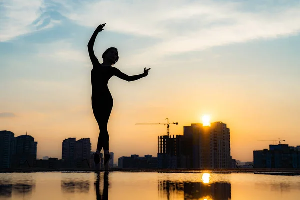 Silueta de bailarina actuando sobre paisaje urbano y dramático fondo de atardecer. Concepto de ternura, ligereza, aireación — Foto de Stock