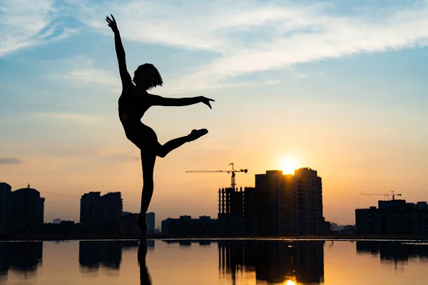 Silueta de bailarina actuando sobre paisaje urbano y dramático fondo de atardecer. Concepto de fuerza de voluntad, control y sueño — Foto de Stock
