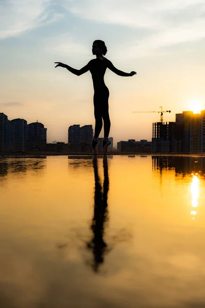 A balerina sziluettje városképpel és drámai naplementével. A gyengédség, a könnyedség és a levegőszerűség fogalma — Stock Fotó