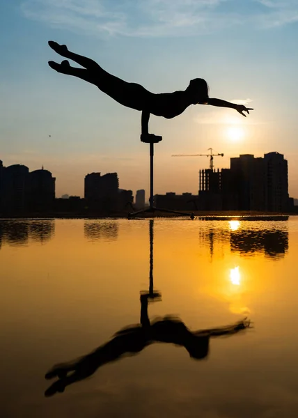 Artista de circo femenino flexible mantener el equilibrio y tocar el sol contra el atardecer dramático y paisaje urbano. Motivación, pasión y concepto de logro — Foto de Stock