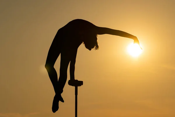 Silhouette di acrobata flessibile che fa manubrio e tocca il disco solare sullo sfondo drammatico del tramonto. Concetto di individualità, creatività ed eccezionale.. — Foto Stock