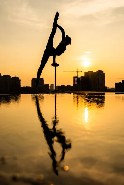 Acróbata flexible haciendo soporte de mano en el fondo del paisaje urbano durante la dramática puesta de sol. Concepto de fuerza de voluntad, control y sueño — Foto de Stock