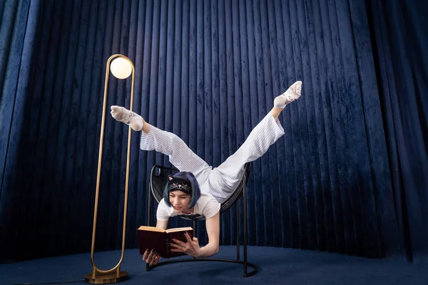 Flexibel ung flicka i pyjamas läsa bok på ett kreativt sätt inomhus. Begreppet individualitet, studier och självutveckling — Stockfoto