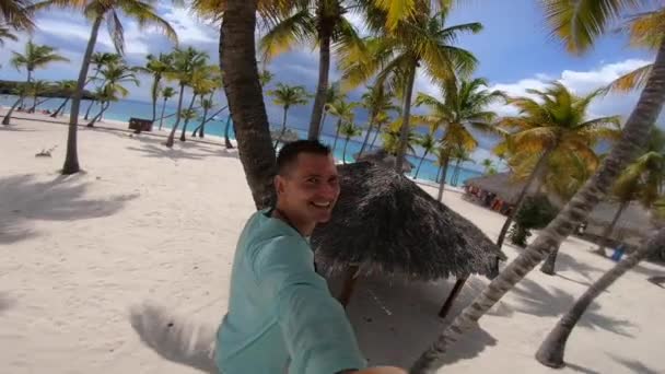 Boldog mosolygós férfi szelfiket készít a parton és pálmafákat. Kaland- és utazási koncepció — Stock videók
