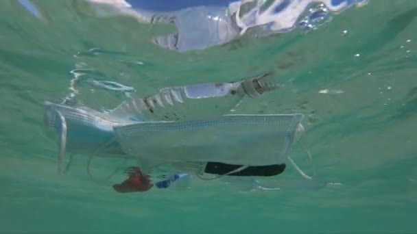 Máscaras protectoras y basura plástica flotando bajo el agua. Contaminación del medio ambiente y concepto de cuestiones ecológicas — Vídeo de stock