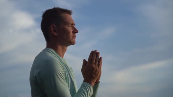 Junger Mann betet und kreuzt sich auf blauem Himmelhintergrund. Religion, Glaube und Hoffnung — Stockvideo