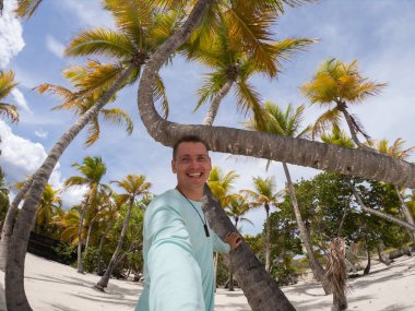 Mutlu gülümseyen adam sahilde palmiye ağaçlarıyla selfie çekiyor. Tatil ve seyahat kavramı 