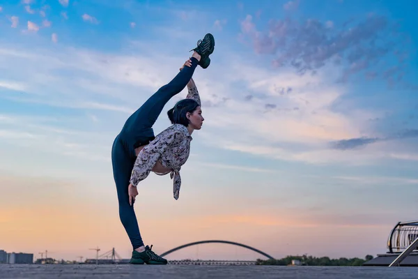 Silueta de mujer de yoga flexible manteniendo el equilibrio en división en dramático atardecer y paisaje urbano. Concepto de estilo de vida saludable y salud — Foto de Stock