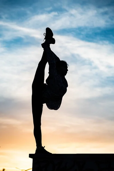 Silueta de mujer de yoga flexible manteniendo el equilibrio en división en la puesta de sol dramática. Concepto de estilo de vida saludable y salud — Foto de Stock