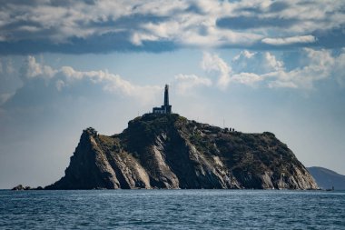 Denizdeki küçük kayalık adanın tepesindeki deniz feneri. Seyahat ve macera kavramı