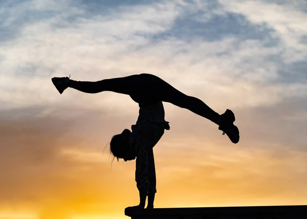 Silueta de gimnasta mujer flexible haciendo handstand en el atardecer dramático. Concepto de individualidad, creatividad y sobresaliente — Foto de Stock