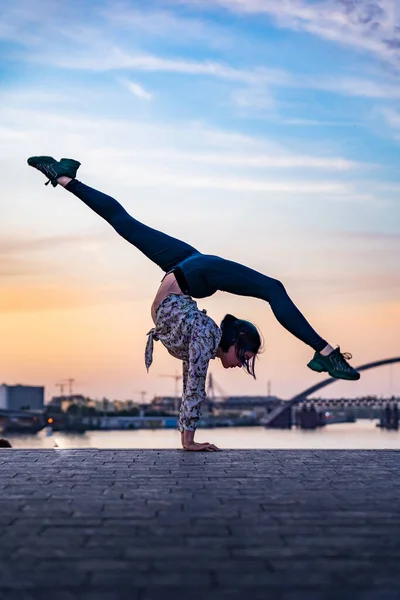 Silueta de artista de circo femenino flexible haciendo handstand en el dramático atardecer y paisaje urbano. Concepto de individualidad, creatividad y sobresaliente — Foto de Stock