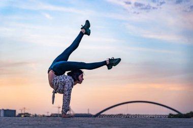 Esnek kadın silueti dramatik günbatımı ve şehir manzarasında amuda kalkıyor. Bireysellik kavramı, yaratıcılık ve olağanüstü