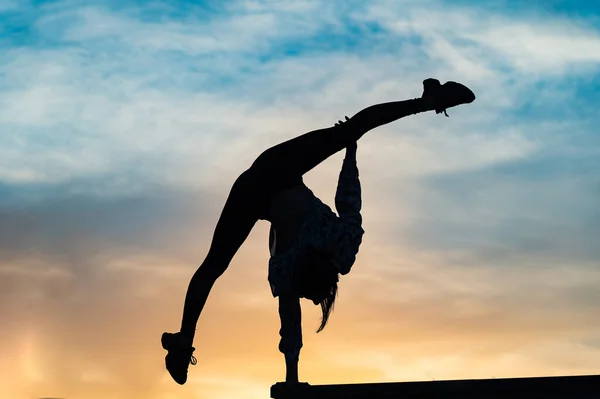 Silueta de acróbata flexible hembra haciendo soporte de mano en la dramática puesta de sol. Concepto de individualidad, creatividad y sobresaliente — Foto de Stock