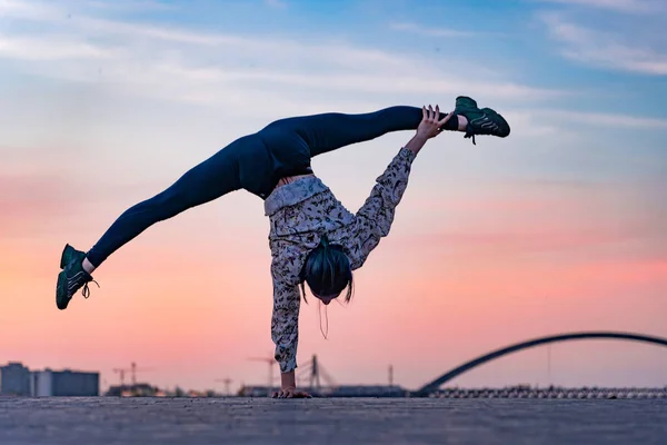 Silueta de artista de circo femenino flexible haciendo handstand en el dramático atardecer y paisaje urbano. Concepto de individualidad, creatividad y sobresaliente — Foto de Stock
