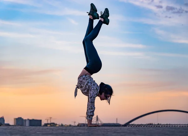 Silueta de mujer flexible haciendo handstand en el dramático atardecer y paisaje urbano. Concepto de fuerza de voluntad, motivación y estilo de vida saludable — Foto de Stock