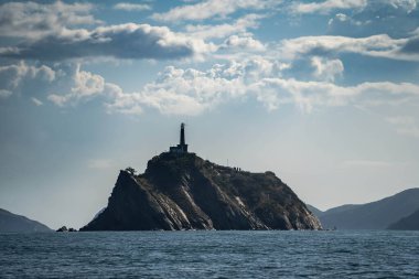 Denizdeki küçük kayalık adanın tepesindeki deniz feneri. Seyahat ve macera kavramı
