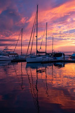 Marina 'nın sakin sularında, yelkenlilerin üzerinde dramatik bir gün batımı. Seyahat ve macera konsepti 