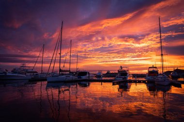 Marina 'nın sakin sularında, yelkenlilerin üzerinde dramatik bir gün batımı. Seyahat ve macera konsepti 