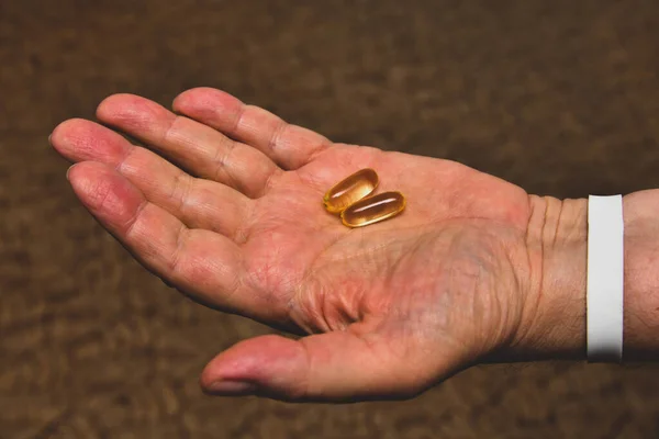 Yaşlı bir adam elinde D vitamini, balık yağı ve Omega kapsülleri tutar.