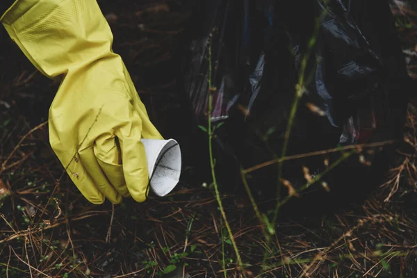 Eco-activist, environmental volunteer wearing yellow gloves removes trash into a garbage bag