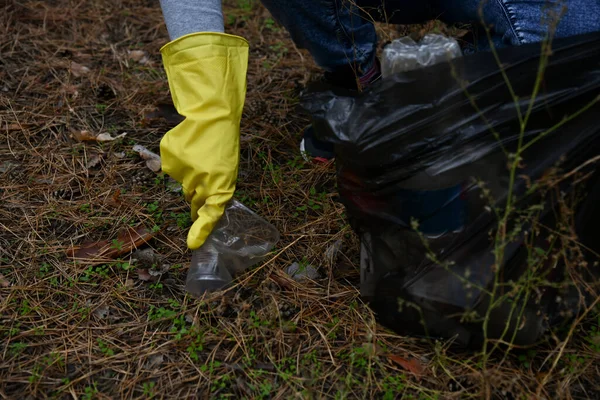 Eco-activist, climate activist, environmental volunteer wearing yellow gloves removes trash into a garbage bag