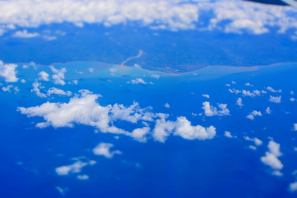 Вид с воздуха из окна самолета, облачность, земля сверху, океан, море и побережье
