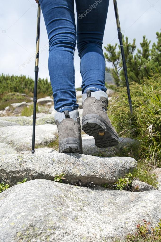 Hiking woman with trekking boots and sticks on the rocky trail