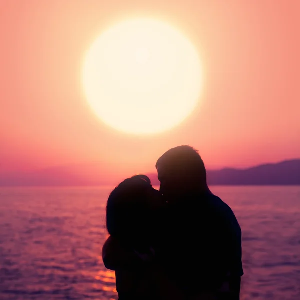 Fiatal pár élvezi a naplementét a strandon. csók. Sziluettjét a férfi és a nő — Stock Fotó