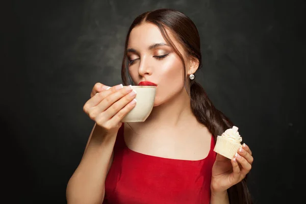 美しい女性はコーヒーを飲み 黒の背景にカップケーキを食べる — ストック写真