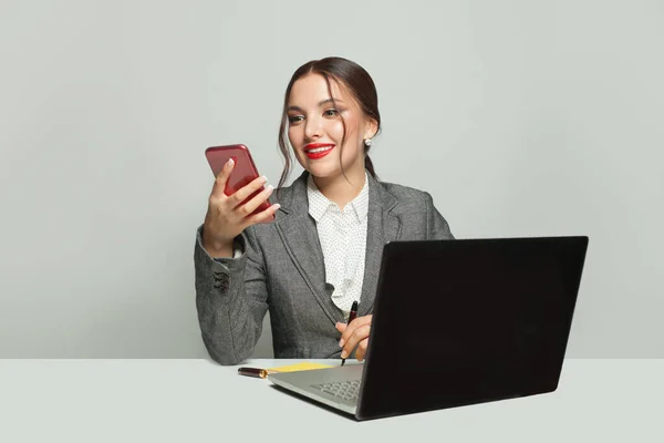 带着手提电脑和电话坐在办公室里的快乐女商人 — 图库照片