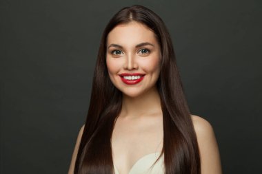 Gülümseyen esmer model, uzun düz saç ve siyah arka planda sevimli bir gülümseme.