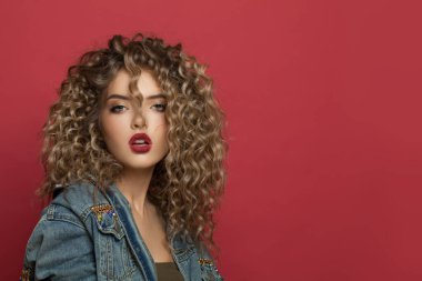 Kırmızı arka planda kıvırcık saçlı çekici manken kadın.