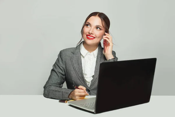 办公室里坐着一个带着笔记本电脑和电话的快乐的女商人 — 图库照片