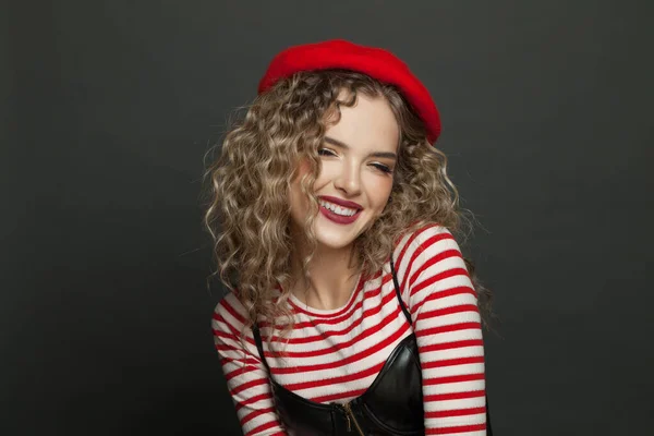 黒の壁の背景に縞模様のTシャツと赤のフランススタイルのベレー帽の陽気な女性 — ストック写真