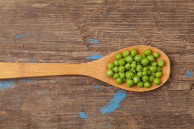 Tahta arka planda kaşık içinde yeşil bezelyeler