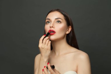 Güzel bir kadın siyah arka planda ruj sürüyor.