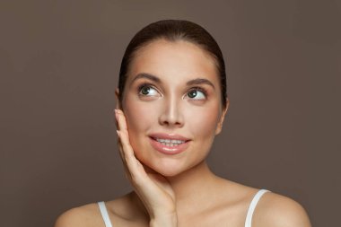 Açık tenli, gülümseyen ve yukarı bakan neşeli genç bir kadın. Cilt bakımı ve yüz tedavisi kavramı