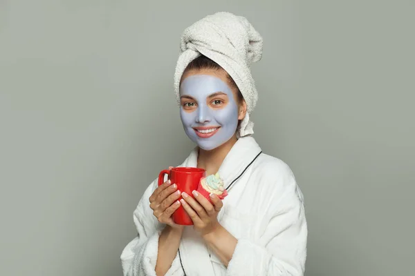 Young happy woman in cosmetic face mask eating breakfast and drinking coffee. Female day routine