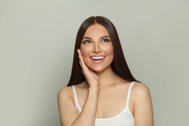 Açık tenli, uzun ve sağlıklı düz saçlı mutlu esmer model kadın. Cilt bakımı ve yüz tedavisi kavramı