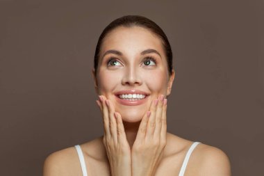 Mükemmel gülüşü ve kahverengi arka planda manikürlü tırnakları olan güzel, şaşkın bir kadın.